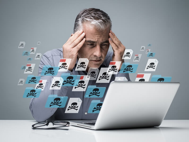 un homme qui se tiens la tête devant son ordinateur d'où sorte des virus symbolisé par des têtes de mort