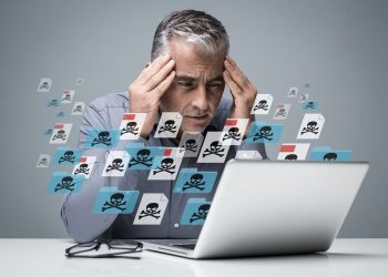 un homme qui se tiens la tête devant son ordinateur d'où sorte des virus symbolisé par des têtes de mort